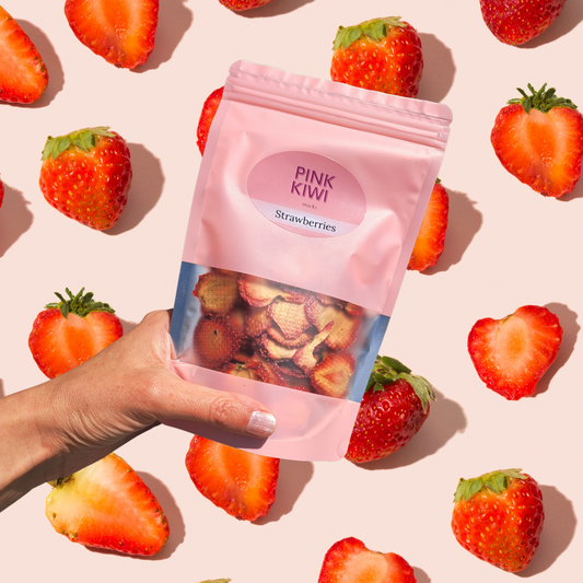 Hand holding a Pink Kiwi dried strawberries snack pouch with a playful strawberry background, highlighting healthy and delicious freeze-dried fruit snacks.