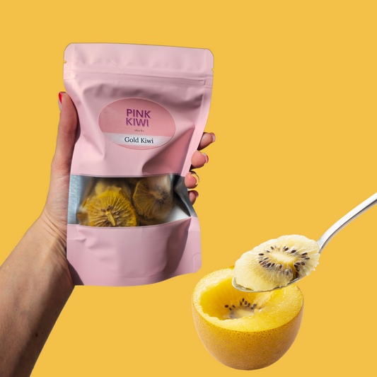 Hand holding a pack of Pink Kiwi Gold Kiwi dried fruit with a fresh golden kiwi being scooped on the side, displayed on a vibrant yellow background.
