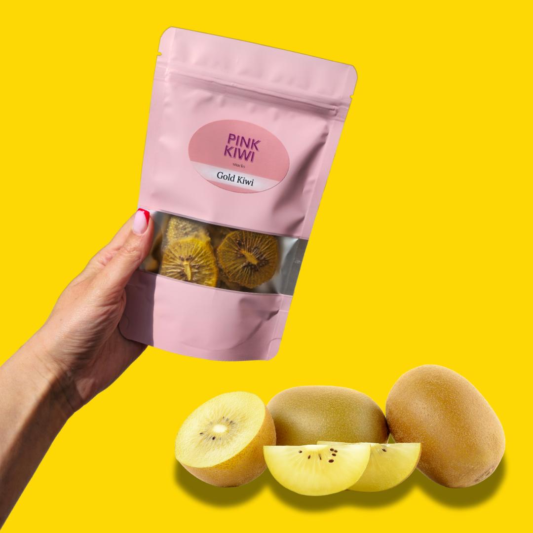 Hand holding Pink Kiwi Gold Kiwi dried fruit snack pouch with fresh sliced golden kiwis displayed on a bright yellow background