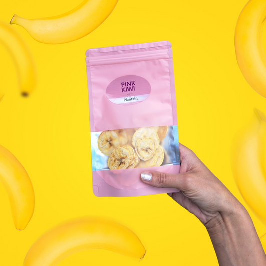 Hand holding a Pink Kiwi Snacks pouch of dried plantain slices against a vibrant yellow background with floating bananas.