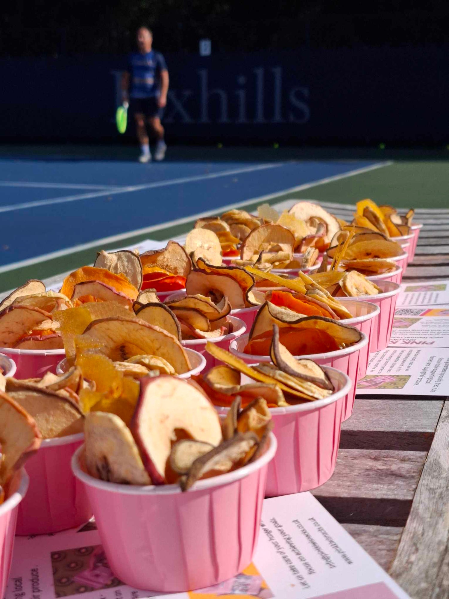 Pink Kiwi Snacks' dried fruit cups displayed courtside at a 2024 tennis tournament, promoting healthy snacking.