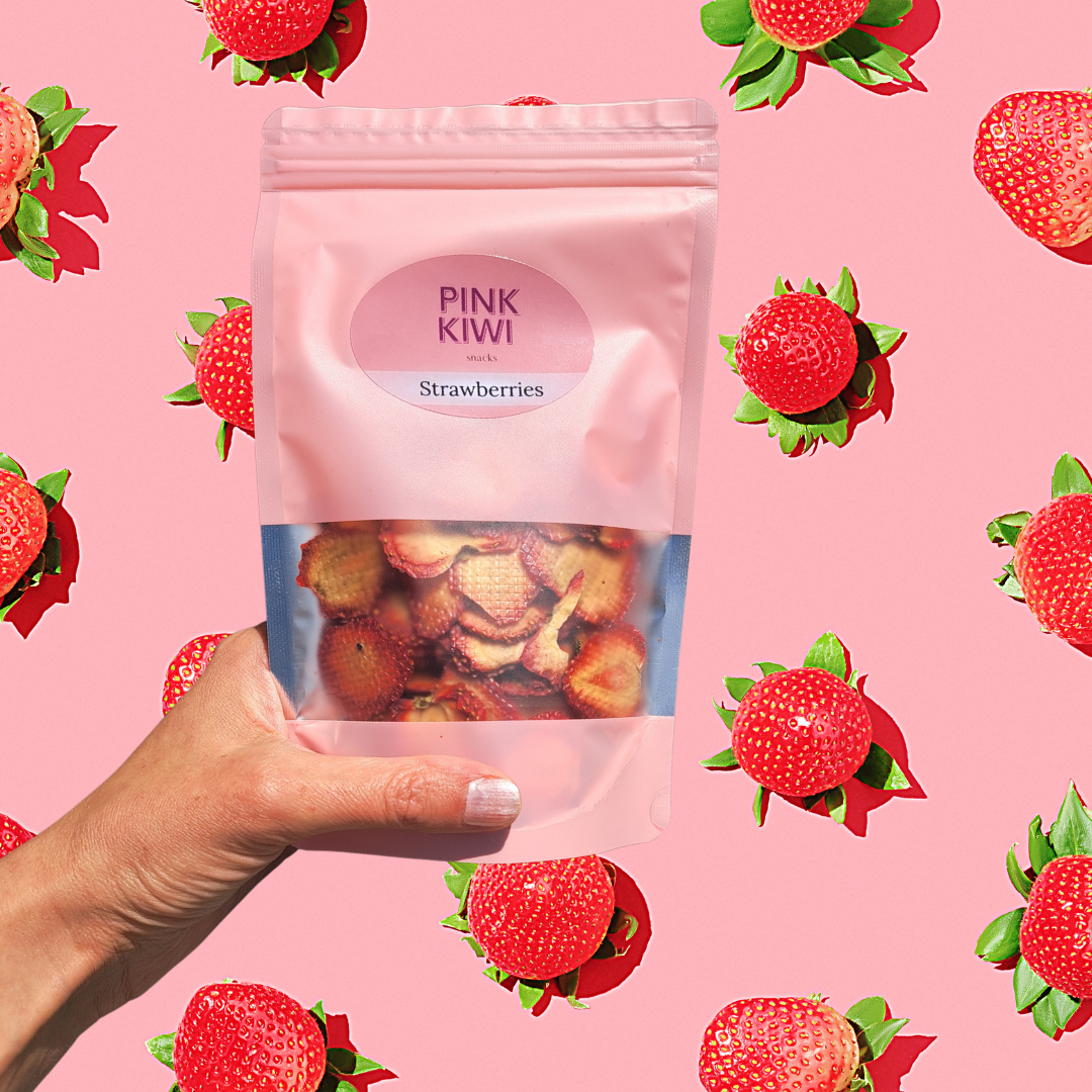 Hand holding a Pink Kiwi dried strawberries snack pouch against a bright strawberry-patterned background, showcasing tasty and nutritious fruit snacks.