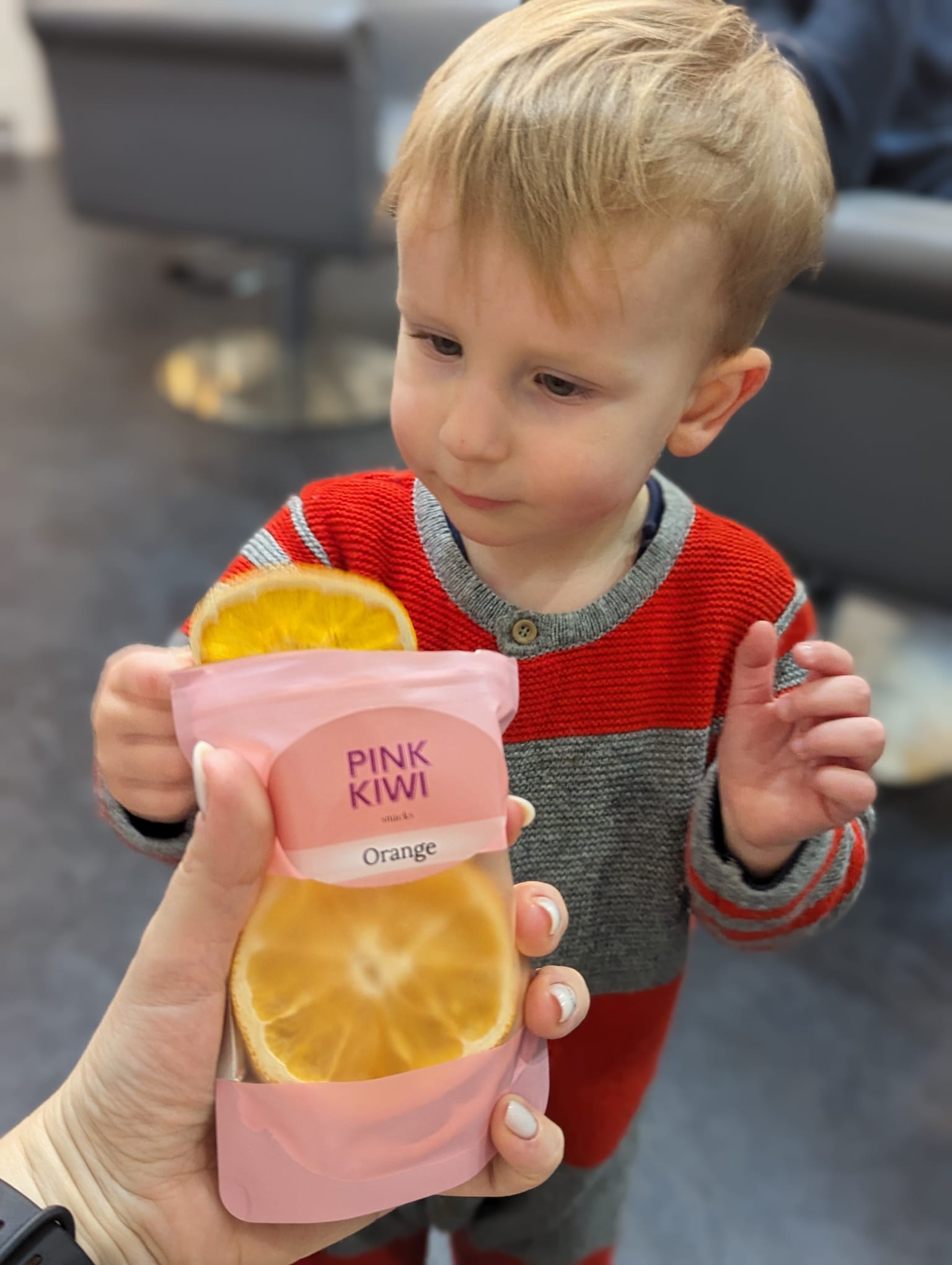 Young child reaching for Pink Kiwi dried orange snack, promoting healthy eating habits for kids with natural fruit snacks.