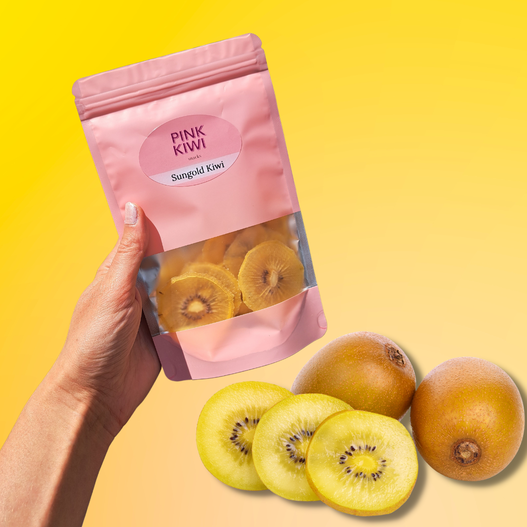 Hand holding Pink Kiwi dried Sungold Kiwi snack pack with fresh golden kiwis on a yellow gradient background, showcasing nutritious and vibrant healthy snacking.